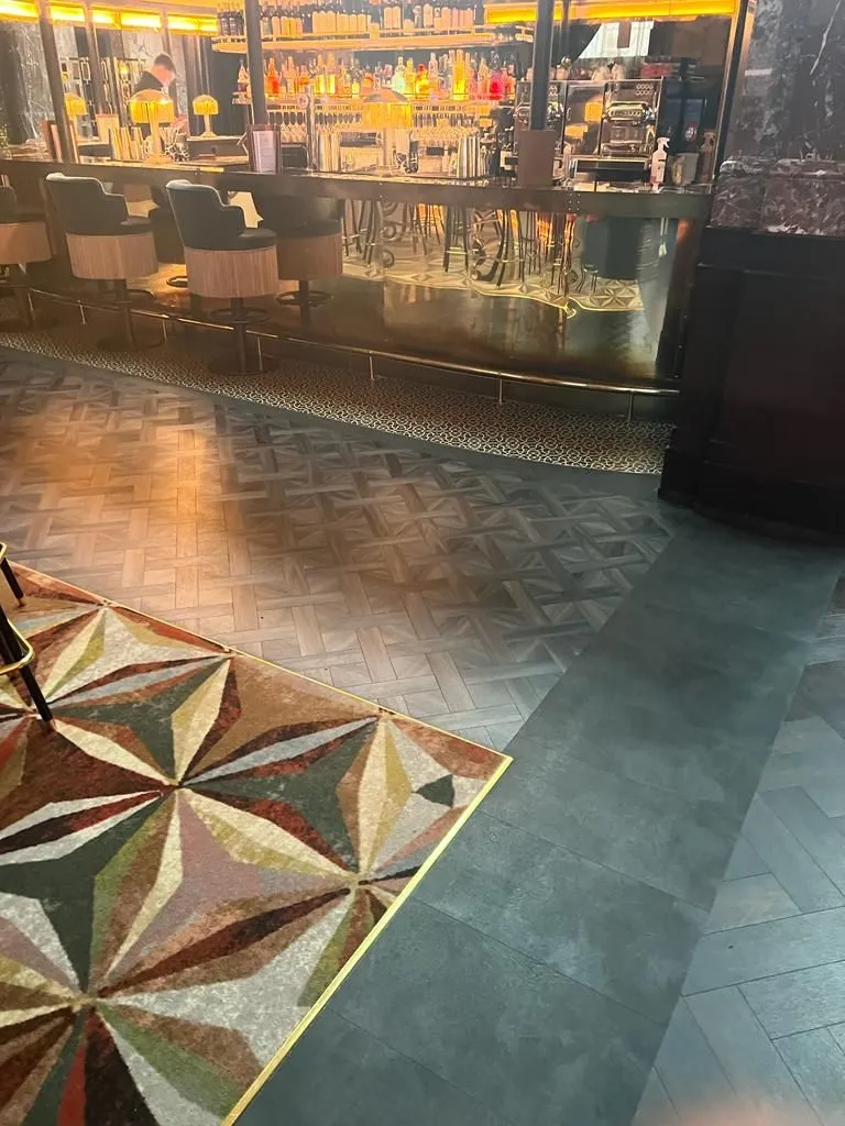 Basket-weave Amtico in front of the main bar, between a brass-edged inset carpet and a dark tile-effect vinyl border, at Gaucho Liverpool